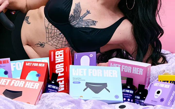 Person with tattooed chest in front of colorful LGBTQ Wet For Her product boxes