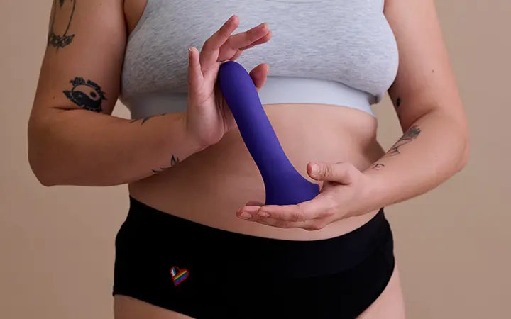 Person wearing an underwear-style black harness holding a purple WondHer