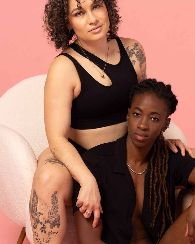 Two lesbian women posing together against a pink background